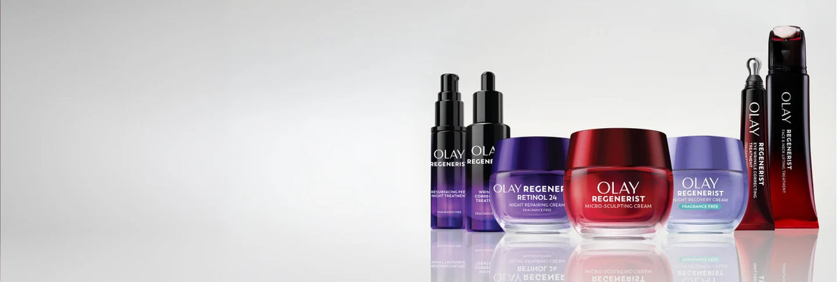 A lineup of Olay Regenerist skincare products on a reflective light gray surface against a white background, including black pump bottles, a purple jar, a red jar, and a red tube.