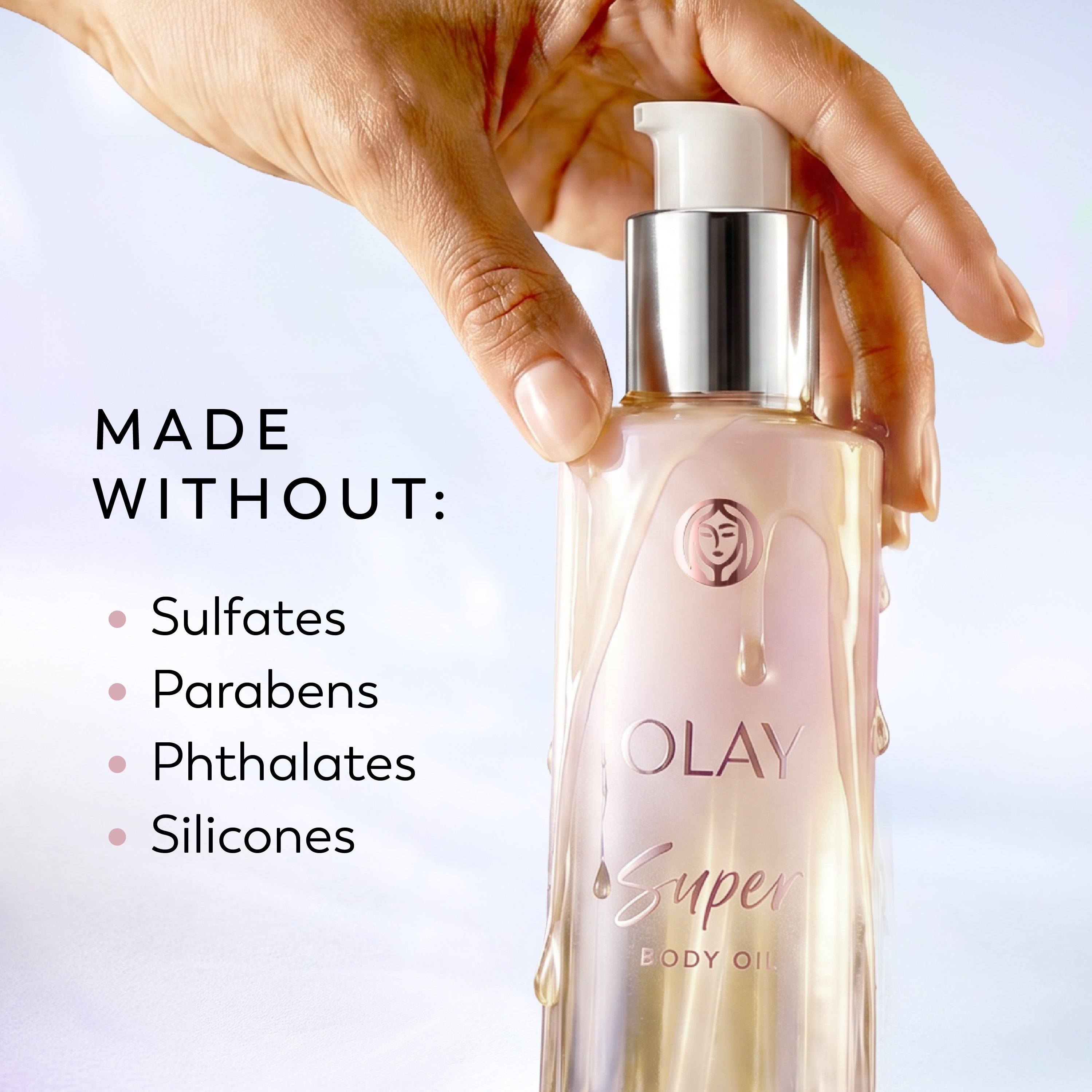 A hand holds a bottle of Olay Super Body Oil against a soft light background, with text on the left reading 'MADE WITHOUT: Sulfates, Parabens, Phthalates, Silicones'.