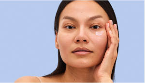 Woman applying skincare product on her face against a blue background