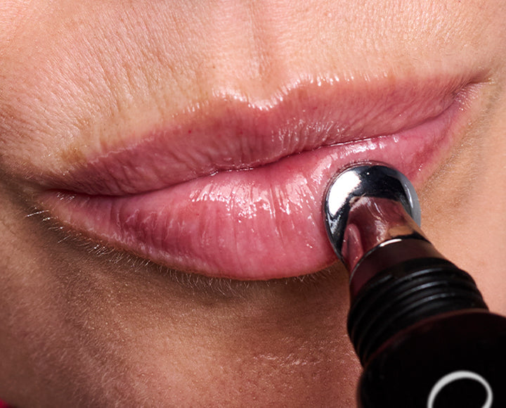 Close-up of a person applying lip gloss to their lips.
