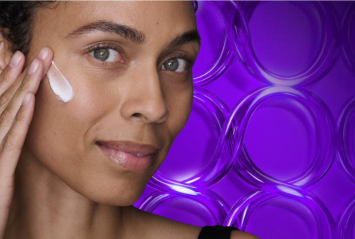 Woman applying cream to her face with a purple circular pattern in the background