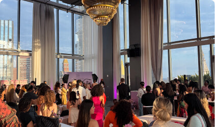 Guests gathered at an indoor Olay event with large windows overlooking the city.