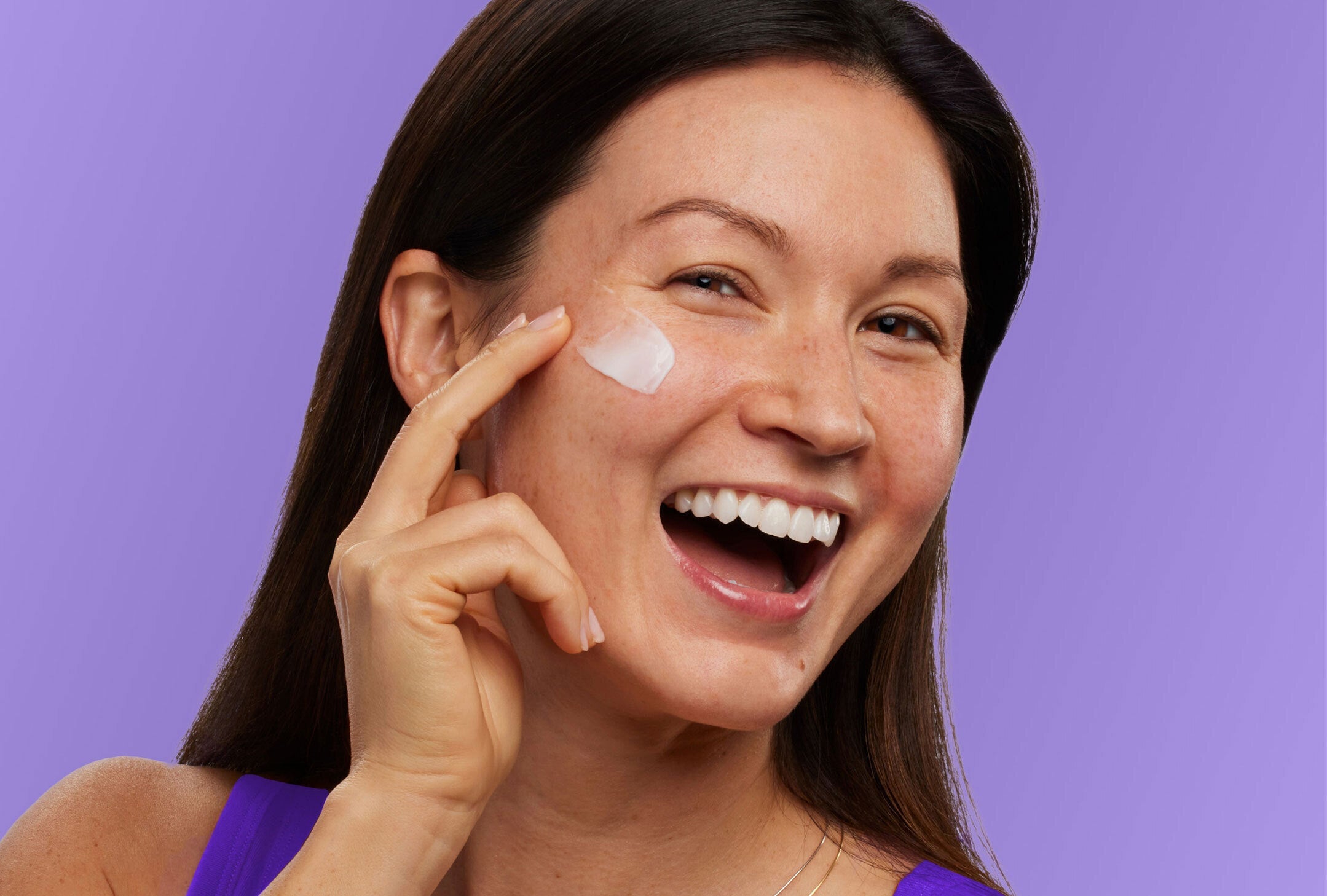 Woman applying cream to her face with a purple background