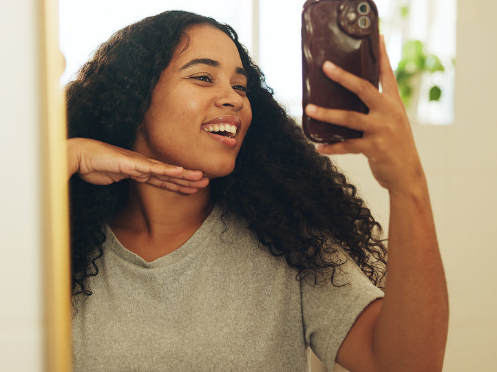 Young woman smiling and posing her face at an angle while holding up her phone to take a selfie photo
