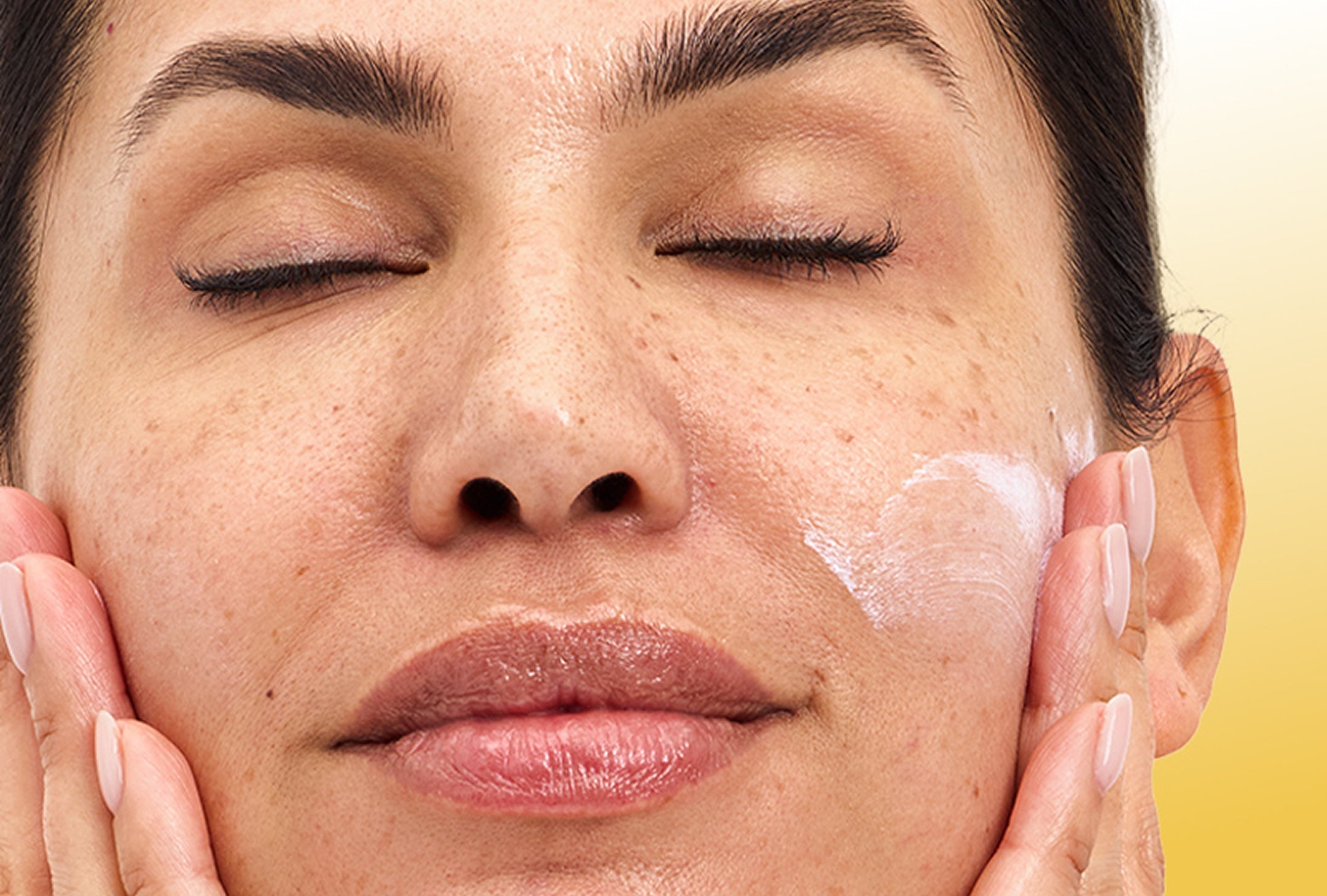 Woman applying cream to her face with a yellow background
