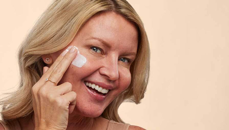 Woman applying cream to her face with a beige background