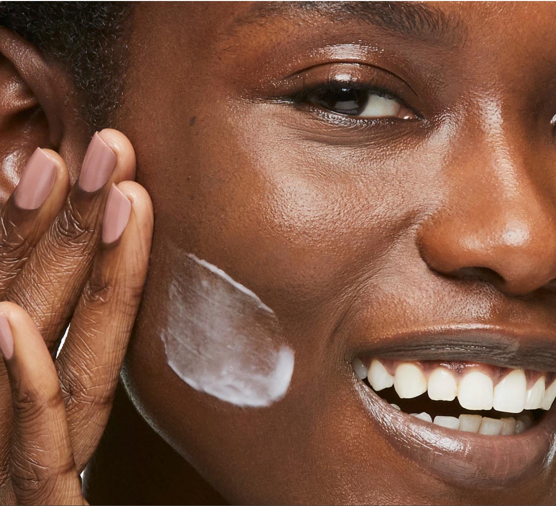 Close-up of a person applying cream to their face with a neutral background